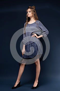 A cute young girl in a blue knitted dress on a blue background with a haircut and curly long hair.