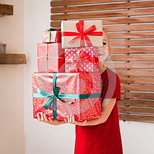 Cute young girl carrying stack of christmas presents, smiling. Happy kid at christmas.