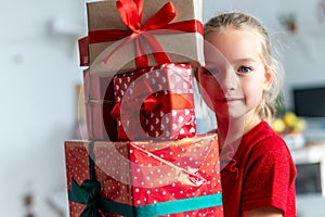 Cute young girl carrying stack of christmas presents, smiling and looking at camera. Happy kid at christmas.