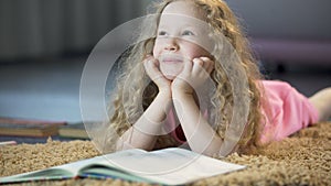 Cute young girl dreaming about happy future, lying on soft carpet at home