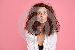 Cute young girl with foxy curly hair making funny face over pink background. Copy space