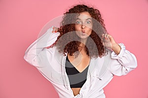 Cute young girl with foxy curly hair making funny face over pink background. Copy space