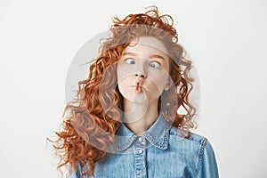 Cute young girl with foxy curly hair making funny face over white background. Copy space.