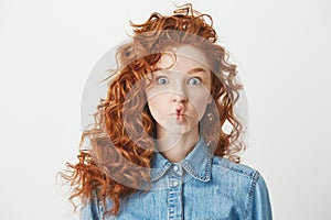 Cute young girl with foxy curly hair making funny face over white background. Copy space.