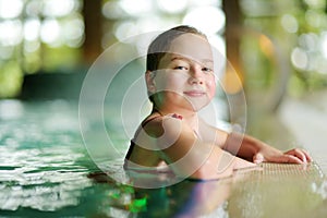 Cute young girl having fun in indoor pool. Child learning to swim. Kid having fun with water toys. Family fun in a pool