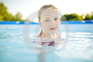 Cute young girl having fun in outdoor pool. Child learning to swim. Kid having fun with water toys. Family fun in a pool