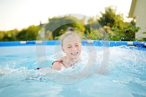 Cute young girl having fun in outdoor pool. Child learning to swim. Kid having fun with water toys. Family fun in a pool