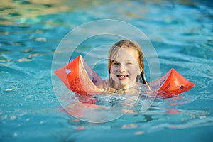 Cute young girl having fun in outdoor pool. Child learning to swim. Kid having fun with water toys. Family fun in a pool. Summer