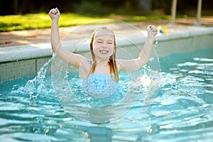 Cute young girl having fun in outdoor pool. Child learning to swim. Kid having fun with water toys. Family fun in a pool. Summer