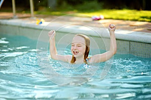 Cute young girl having fun in outdoor pool. Child learning to swim. Kid having fun with water toys. Family fun in a pool. Summer