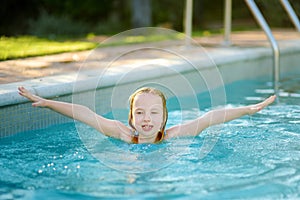 Cute young girl having fun in outdoor pool. Child learning to swim. Kid having fun with water toys. Family fun in a pool. Summer