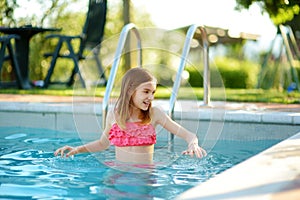 Cute young girl having fun in outdoor pool. Child learning to swim. Kid having fun with water toys. Family fun in a pool. Summer