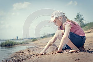 Cute young girl having fun on a sandy lake beach on warm and sunny summer day. Young girl playing by the river. Summer activities