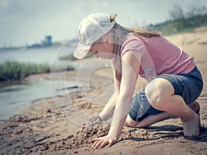 Cute young girl having fun on a sandy lake beach on warm and sunny summer day. Young girl playing by the river. Summer activities