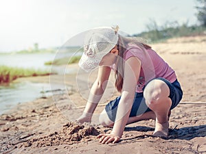 Cute young girl having fun on a sandy lake beach on warm and sunny summer day. Young girl playing by the river. Summer activities