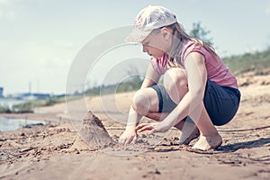 Cute young girl having fun on a sandy lake beach on warm and sunny summer day. Young girl playing by the river. Summer activities