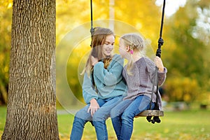 Cute young girl having fun on a swing in sunny autumn park. Family weekend in a city