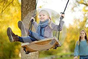 Cute young girl having fun on a swing in sunny autumn park. Family weekend in a city