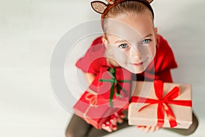 Cute young girl holding christmas presents, smiling and looking at camera. Happy kid at christmas time sitting on the floor.