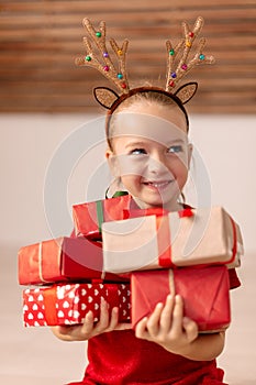 Cute young girl holding stack of christmas presents, smiling and looking away from camera. Happy kid at christmas time.