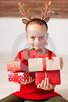 Cute young girl holding stack of christmas presents, smiling and looking at camera. Happy kid at christmas.