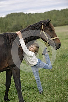 Cute young girl hugging beautiful horse's neck and looking at the camera. Lifestyle portrait