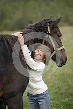 Cute young girl hugging beautiful horse's neck and looking at the camera. Lifestyle portrait