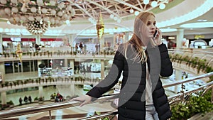 Cute young girl in jacket, talking on a cell phone, ending the call in a big shopping center.