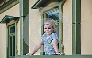 A cute young girl leans on the railing with balusters on the porch of an old building