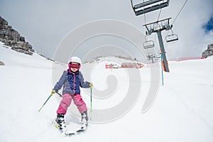 Cute young girl learning to ski at winter resort on a sunny day.