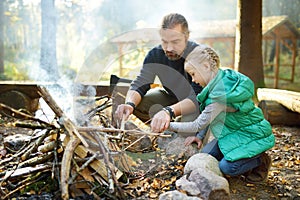 Cute young girl learning to start a bonfire. Father teaching her daughter to make a fire. Child having fun at camp fire. Camping