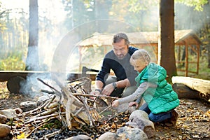 Cute young girl learning to start a bonfire. Father teaching her daughter to make a fire. Child having fun at camp fire. Camping