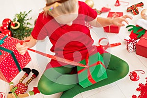 Cute young girl opening christmas present while sitting on living room floor. Candid family christmas time background.