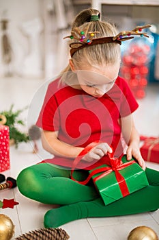 Cute young girl opening christmas present while sitting on living room floor. Candid family christmas time background.