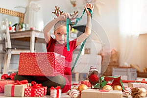 Cute young girl opening large red christmas present while sitting on living room floor. Candid family christmas time. photo