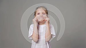 Cute young girl playing the ape. Funny girl showing grimaces over grey background.