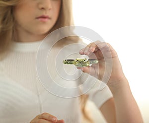 Cute young girl playing with green fidget spinner in bright room - closeup portrait