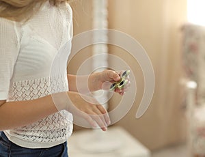 Cute young girl playing with green fidget spinner in bright room - shot with hands