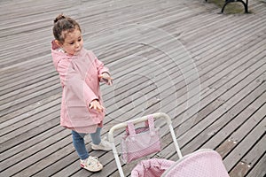 cute young girl playing with her toy stroller on the boarwalk