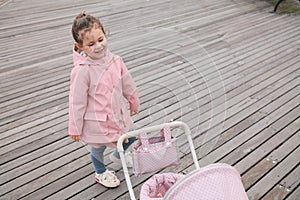 cute young girl playing with her toy stroller on the boarwalk