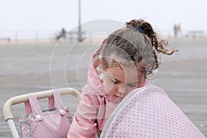 cute young girl playing with her toy stroller on the boarwalk