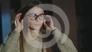 Cute, young girl putting on glasses and smiling at camera in half-light library