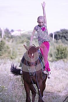 Cute young girl riding a brown horse on a country road at sunset. The child quietly travels on a stallion. The girl confidently