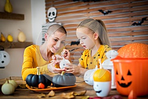 Cute young girl sitting at a table, decorating little white pumpkins with her mother, a cancer patient. DIY Halloween.