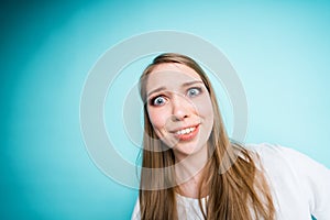 Cute young girl smiling surprised looking at the camera tilting her head and standing on a blue background photo