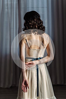 Cute young girl stands in the studio on the background of curtains. Beautiful naked back is visible.