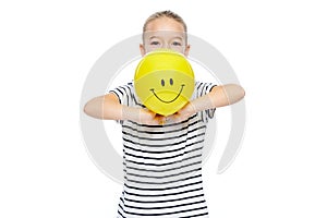 Cute young girl in stripped T-shirt holding yellow balloon with smiley face. Portrait of happy child with balloon.