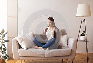 Cute young girl surfing in internet on laptop, resting on couch