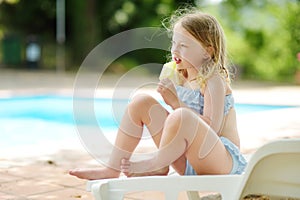 Cute young girl in a swimsuit having an ice cream by outdoor pool. Child having fun on hot summer day. Kid eating gelato on family
