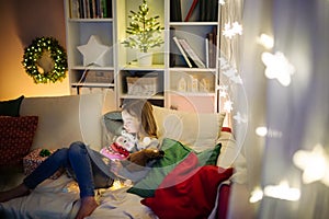 Cute young girl using a tablet pc at home in warm and cozy living room at Christmas. Family having online video call on Xmas eve